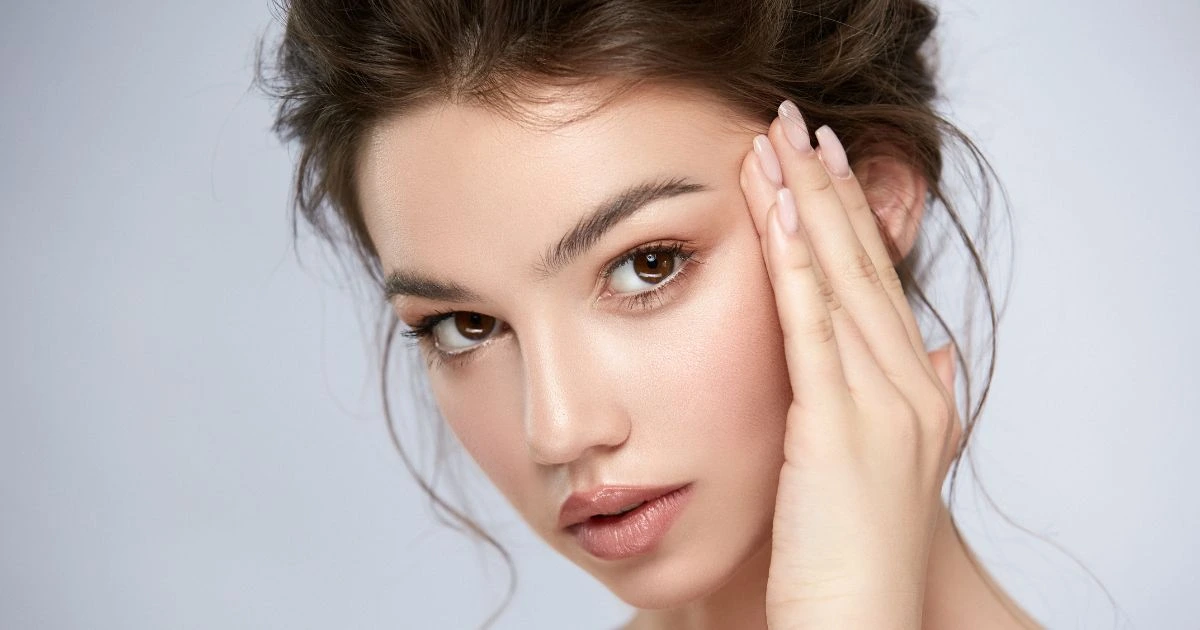 Young woman enjoying flawless, glowing skin after Clearlift treatment, gently touching her face to showcase smooth complexion and natural beauty.